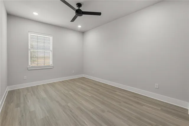 an empty room with wooden floor ceiling fan and windows