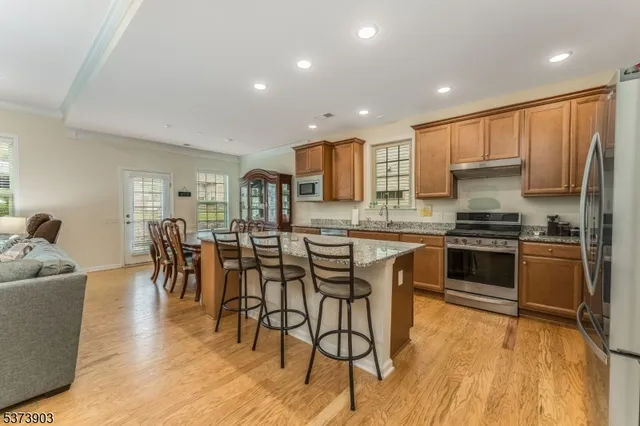 a kitchen with stainless steel appliances kitchen island granite countertop a stove a refrigerator a microwave a dining table and chairs with wooden floor