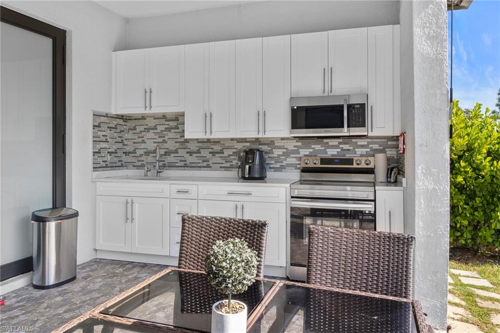 2406 37th Avenue Northeast Naples, FL 34120 - Photo 22 of 29 Kitchen with white cabinetry, stainless steel appliances, light stone countertops, and decorative backsplash
