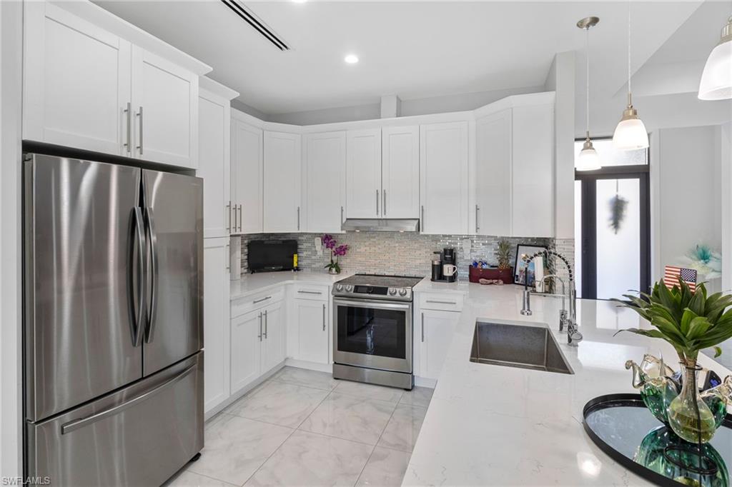 2406 37th Avenue Northeast Naples, FL 34120 - Photo 5 of 29 Kitchen featuring appliances with stainless steel finishes, white cabinets, light stone countertops, tasteful backsplash, and recessed lighting