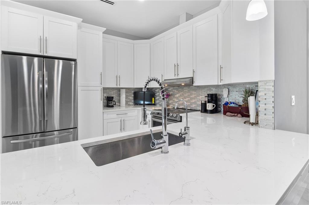 2406 37th Avenue Northeast Naples, FL 34120 - Photo 6 of 29 Kitchen with appliances with stainless steel finishes, light stone countertops, white cabinetry, tasteful backsplash, and pendant lighting