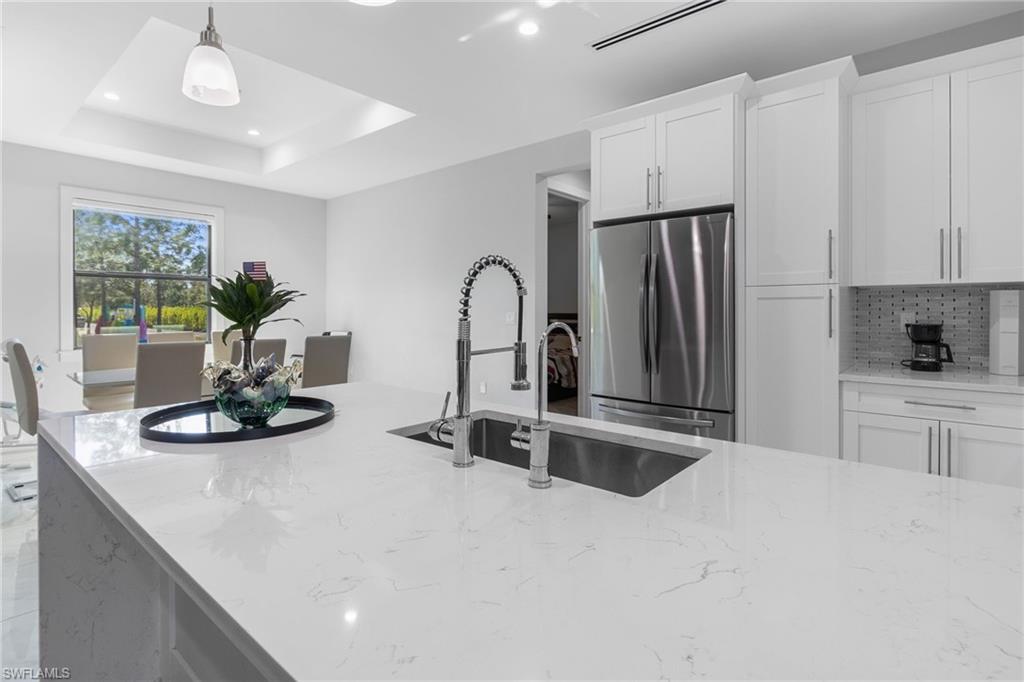 2406 37th Avenue Northeast Naples, FL 34120 - Photo 7 of 29 Kitchen with light stone counters, freestanding refrigerator, pendant lighting, white cabinets, and backsplash