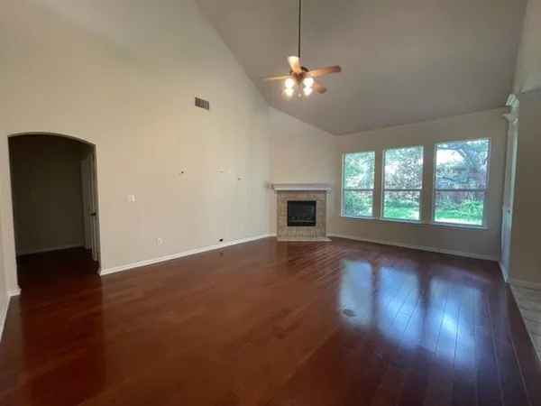 an empty room with wooden floor fireplace and windows