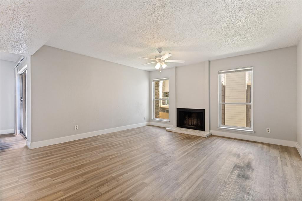 5522 Boca Raton Boulevard, Unit 404 Fort Worth, TX 76112 - Photo 4 of 12 Spacious living area featuring wood-finish flooring, a built-in fireplace with a stone hearth, two large windows, a ceiling fan with integrated lighting, and neutral wall tones