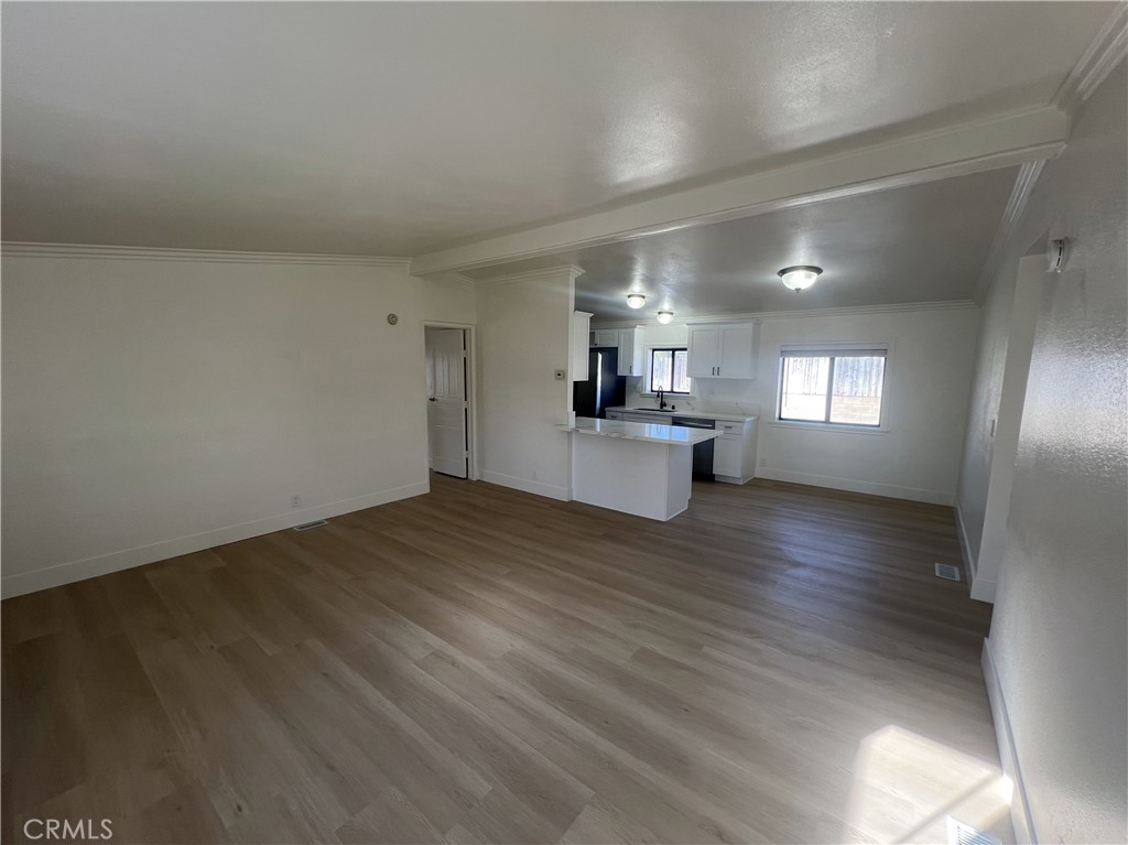 a view of empty room with wooden floor and kitchen view