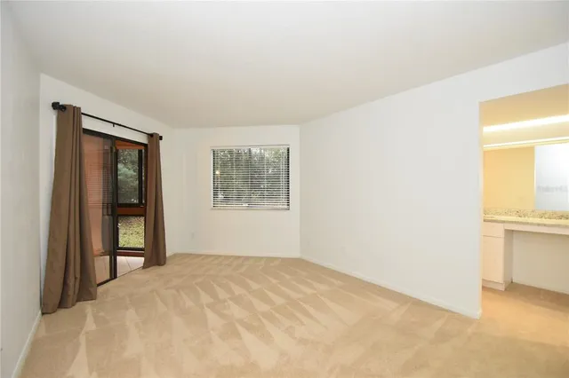 a view of an empty room with window and kitchen view