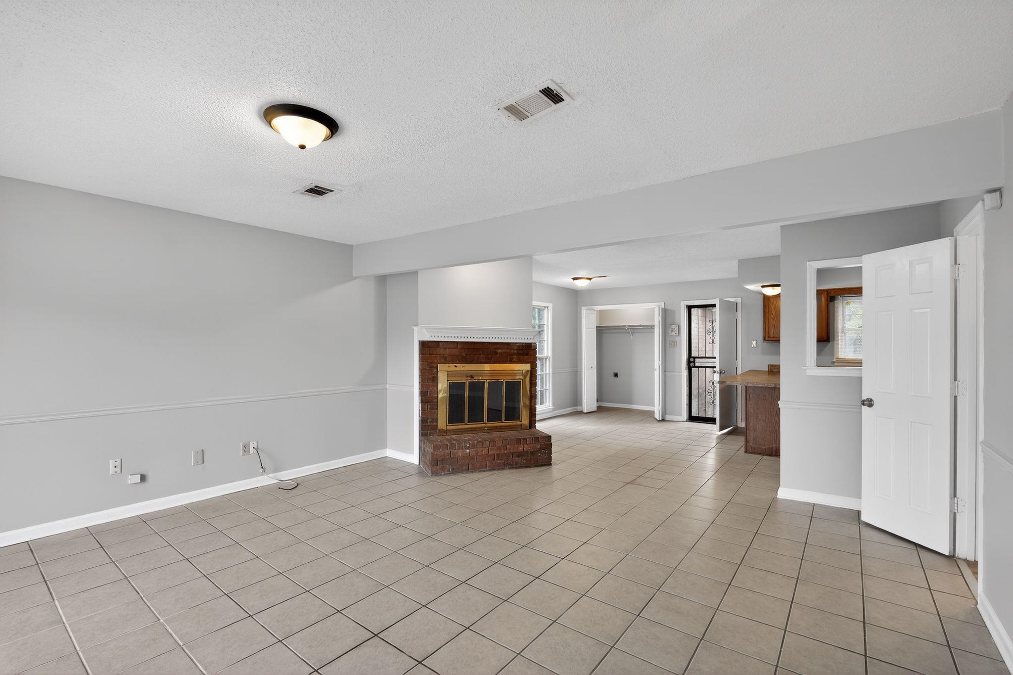 5581 Crepe Myrtle Drive Memphis, TN 38115 - Photo 12 of 33 Unfurnished living room featuring a textured ceiling, a brick fireplace, and light tile patterned flooring