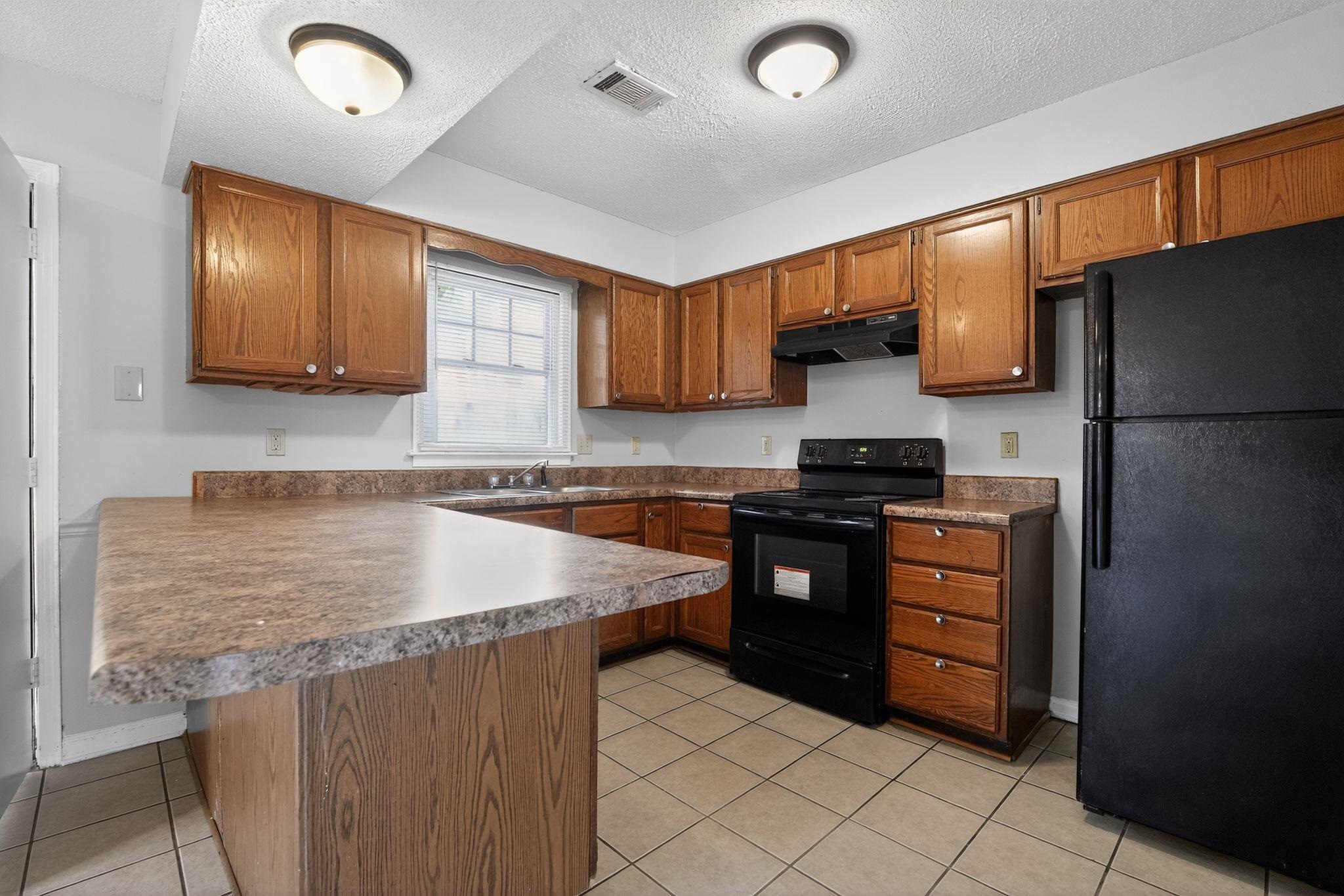 5581 Crepe Myrtle Drive Memphis, TN 38115 - Photo 15 of 33 Kitchen with black appliances, brown cabinetry, a peninsula, a kitchen bar, and a textured ceiling