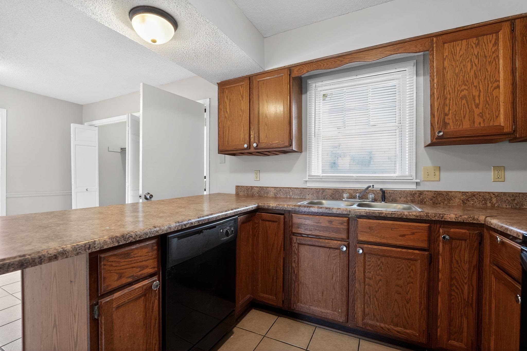 5581 Crepe Myrtle Drive Memphis, TN 38115 - Photo 16 of 33 Kitchen with a peninsula, dishwasher, light tile patterned floors, brown cabinetry, and a textured ceiling