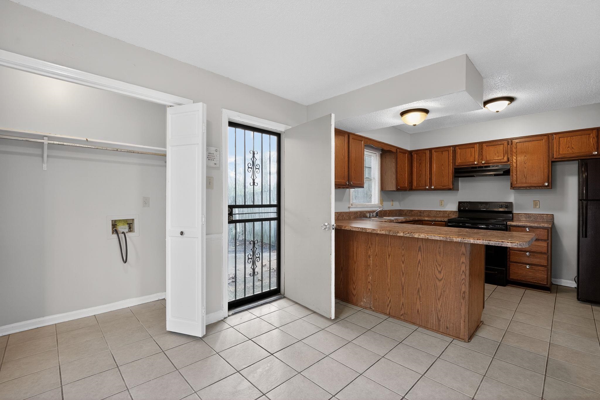 5581 Crepe Myrtle Drive Memphis, TN 38115 - Photo 17 of 33 Kitchen with black appliances, brown cabinets, a peninsula, under cabinet range hood, and light tile patterned flooring