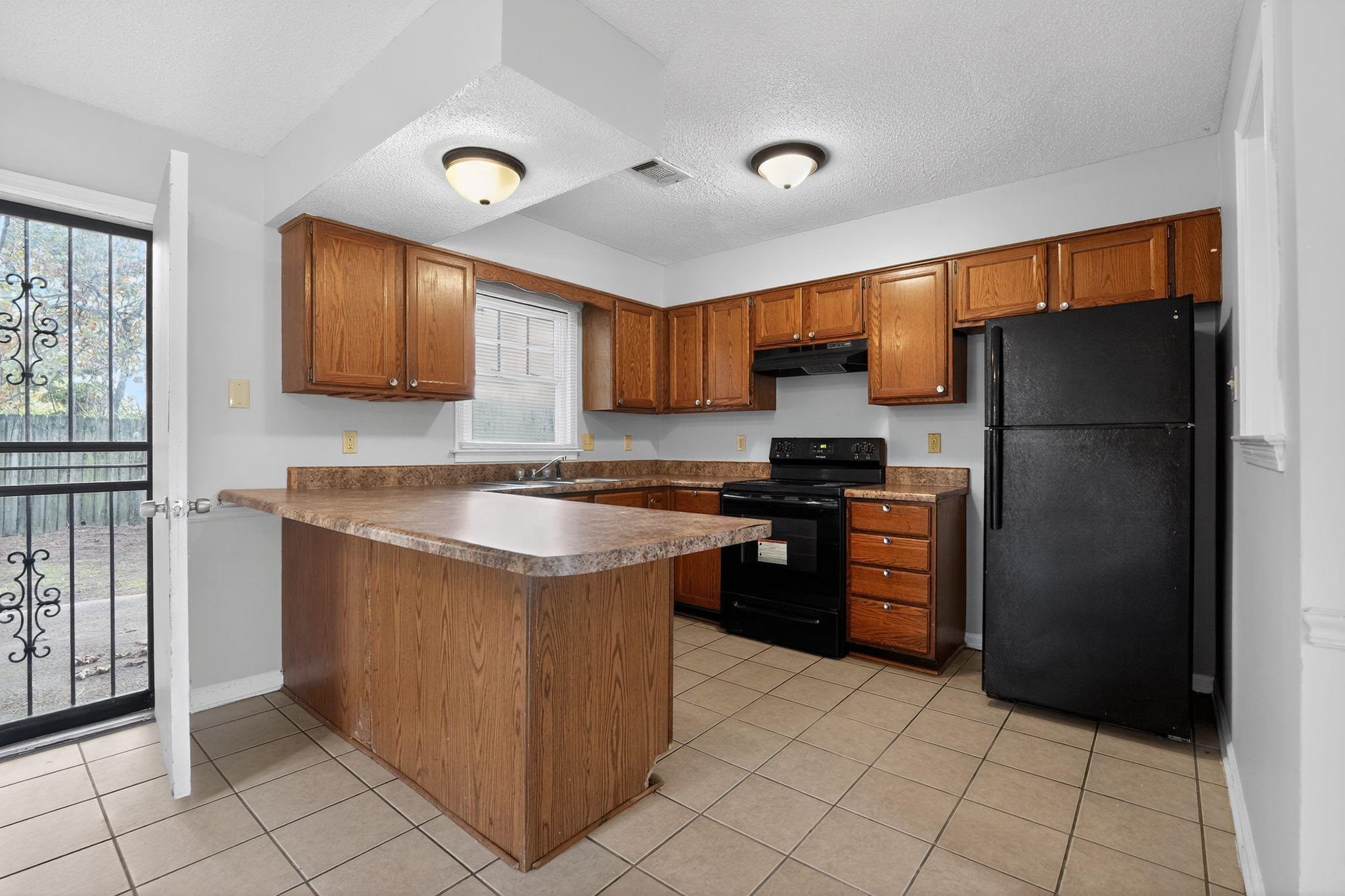 5581 Crepe Myrtle Drive Memphis, TN 38115 - Photo 18 of 33 Kitchen with black appliances, a peninsula, brown cabinets, light tile patterned flooring, and a textured ceiling