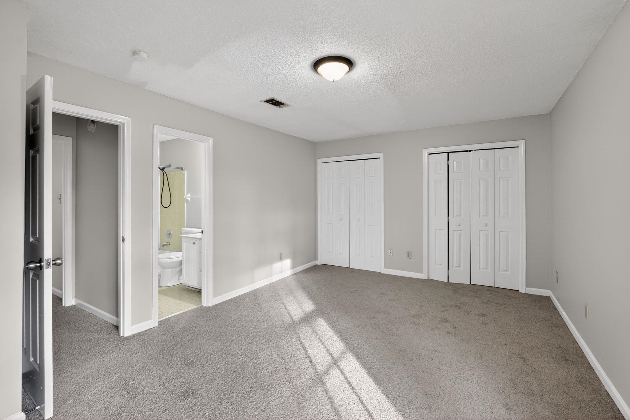 5581 Crepe Myrtle Drive Memphis, TN 38115 - Photo 22 of 33 Unfurnished bedroom featuring multiple closets, light carpet, a textured ceiling, and connected bathroom