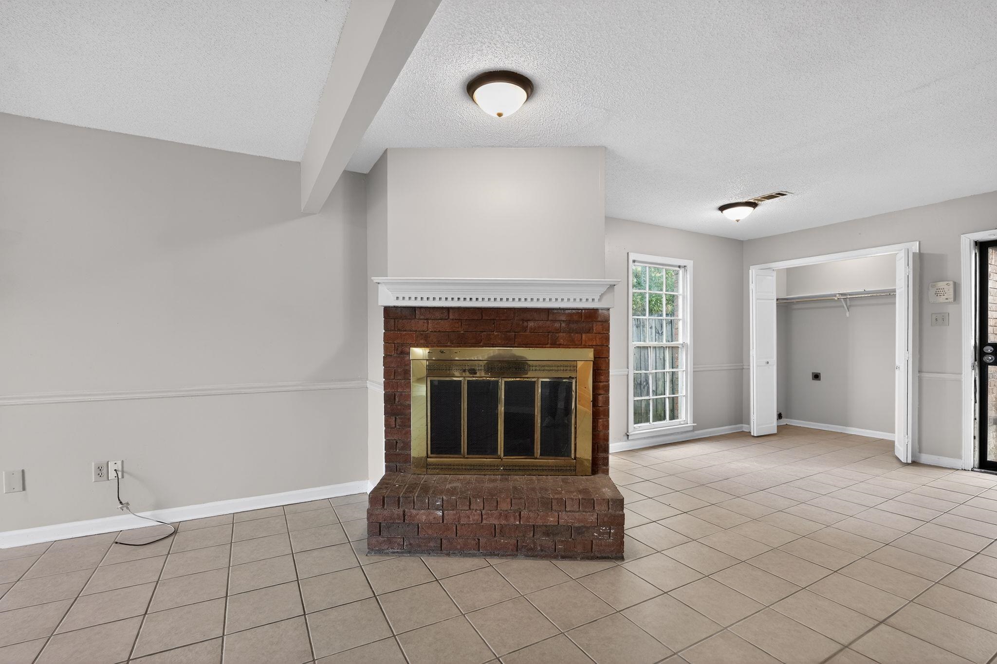 5581 Crepe Myrtle Drive Memphis, TN 38115 - Photo 9 of 33 Unfurnished living room with a brick fireplace, a textured ceiling, and tile patterned floors