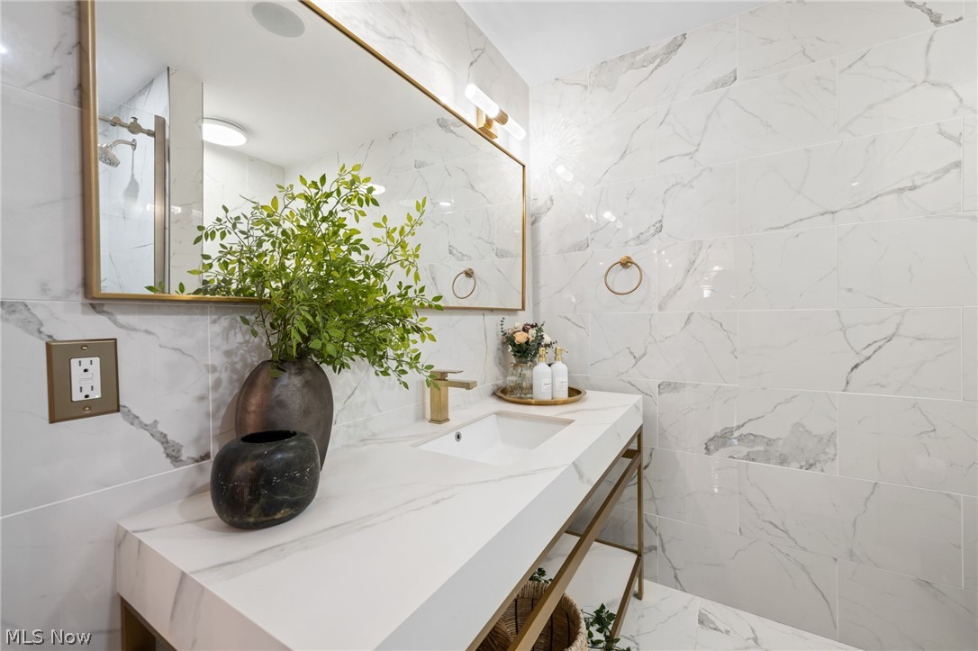25870 Kennedy Ridge Road North Olmsted, OH 44070 - Photo 22 of 50 White marble-style tile walls and flooring in a bathroom featuring a vanity with a white countertop and gold-toned fixtures