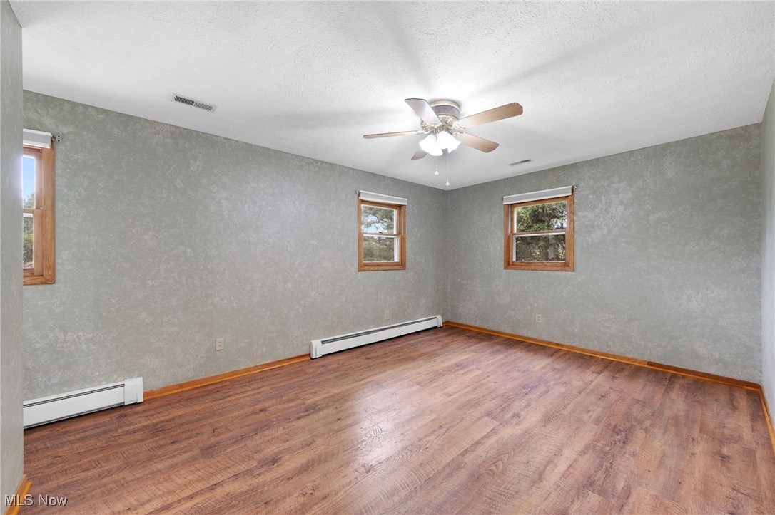 7923 Zigler Road Sterling, OH 44276 - Photo 16 of 31 Spare room with a baseboard radiator, wood finished floors, ceiling fan, and a textured wall