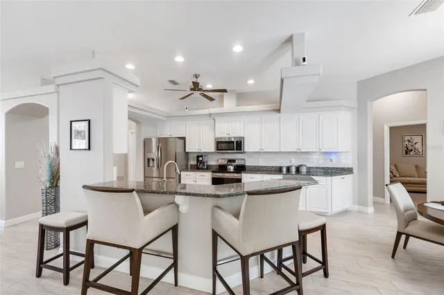 a kitchen with stainless steel appliances granite countertop a refrigerator a stove a sink and white cabinets with wooden floor