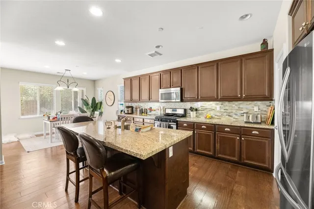 a kitchen with stainless steel appliances granite countertop wooden cabinets a refrigerator a stove a sink and a oven with wooden floor