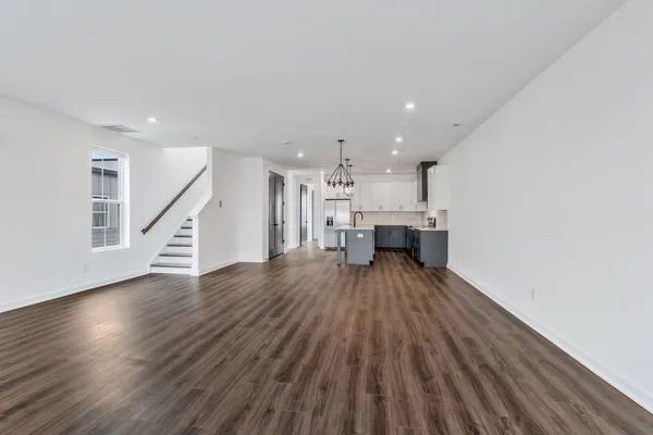 a view of a hallway to an empty room with wooden floor and a kitchen