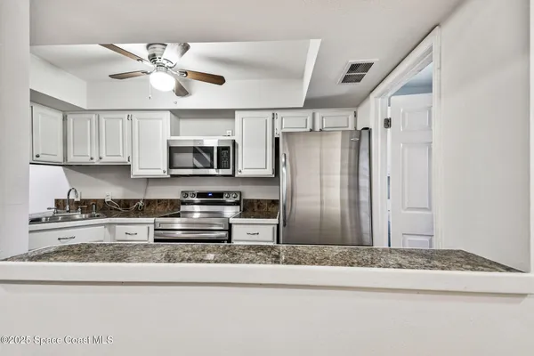 a kitchen with granite countertop white cabinets stainless steel appliances and a counter space