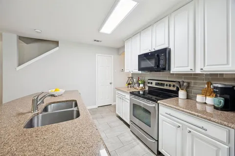 a kitchen with granite countertop a sink a stove top oven and cabinetry