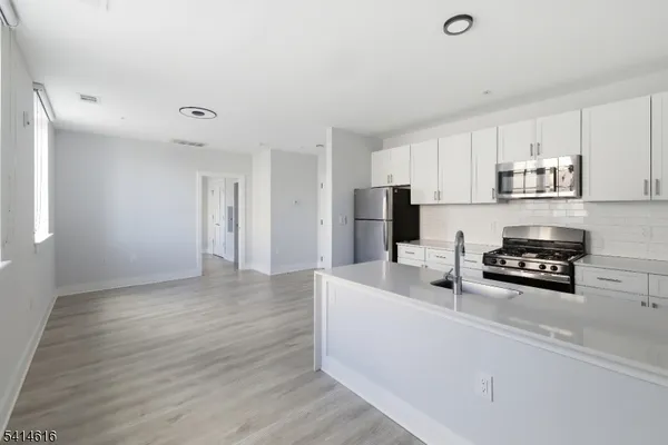 a kitchen with stainless steel appliances a stove a sink a refrigerator white cabinets and wooden floor