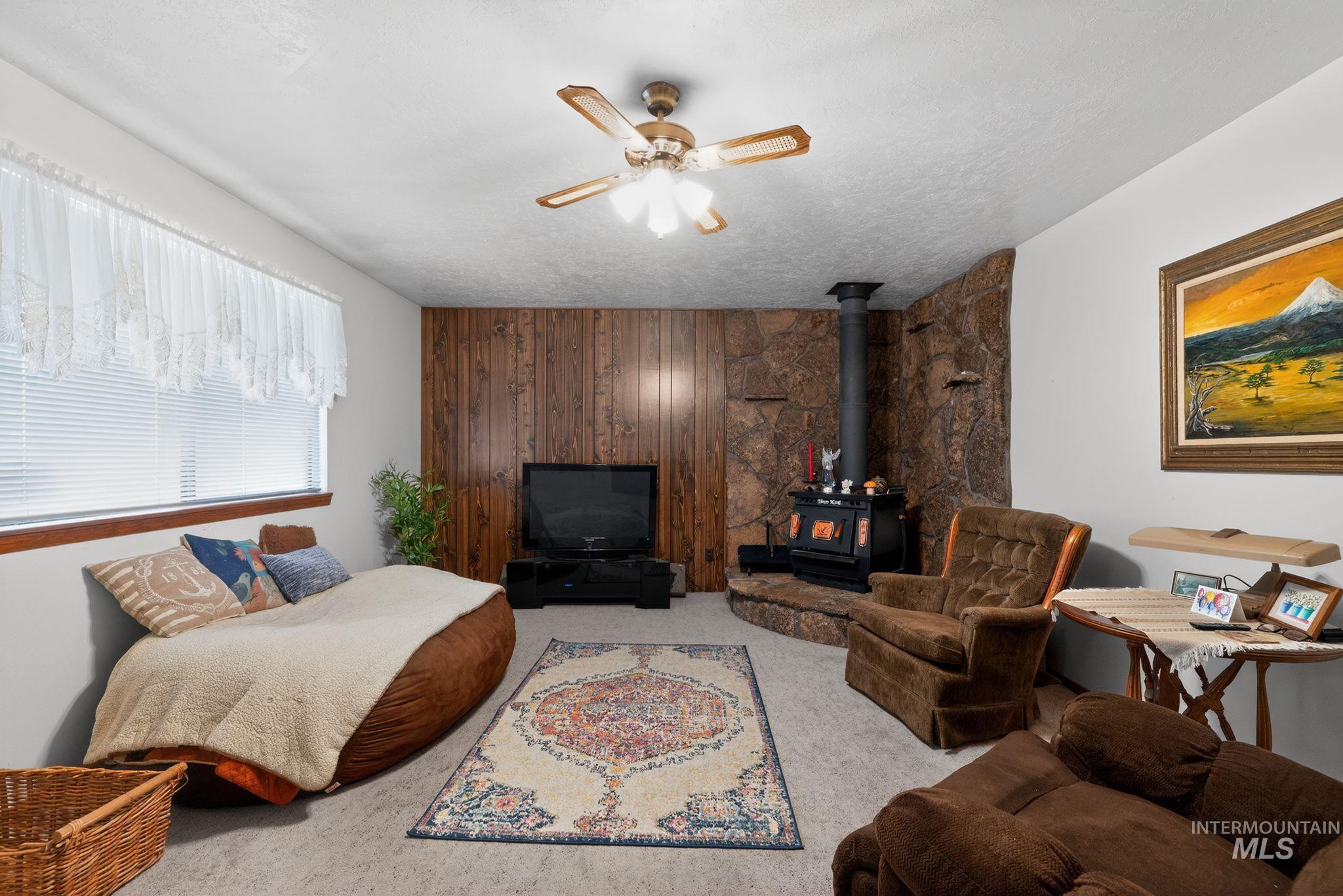 1055 South Adell Street Filer, ID 83328 - Photo 18 of 28 Carpeted bedroom featuring a wood stove, wooden walls, an accent wall, a textured ceiling, and a ceiling fan