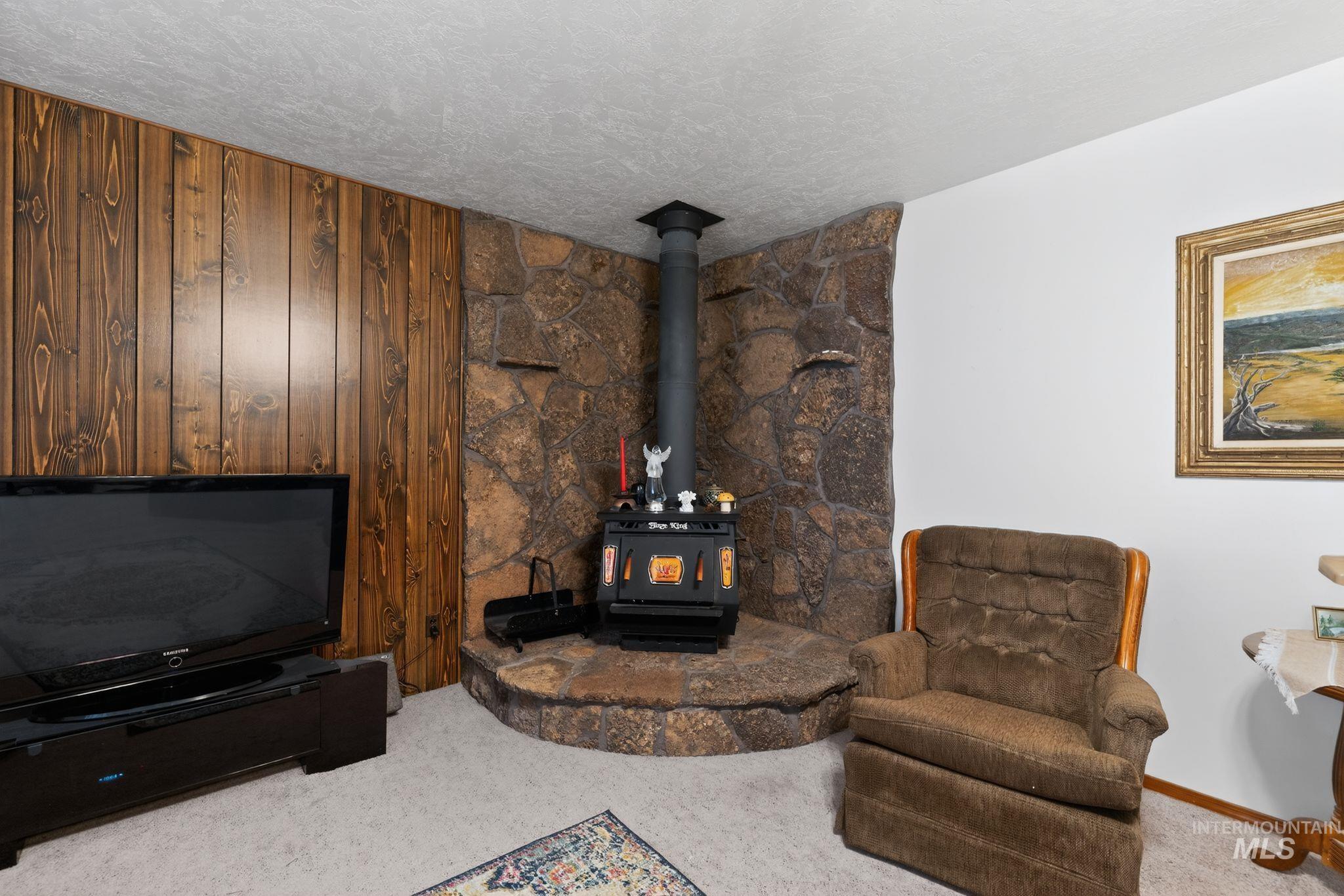 1055 South Adell Street Filer, ID 83328 - Photo 9 of 28 Living area featuring a wood stove, carpet flooring, and a textured ceiling