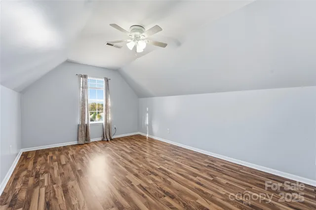 a view of an empty room with wooden floor and a ceiling fan