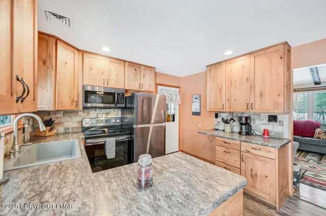 a kitchen with stainless steel appliances granite countertop a refrigerator a sink dishwasher a stove and white countertops with wooden floor