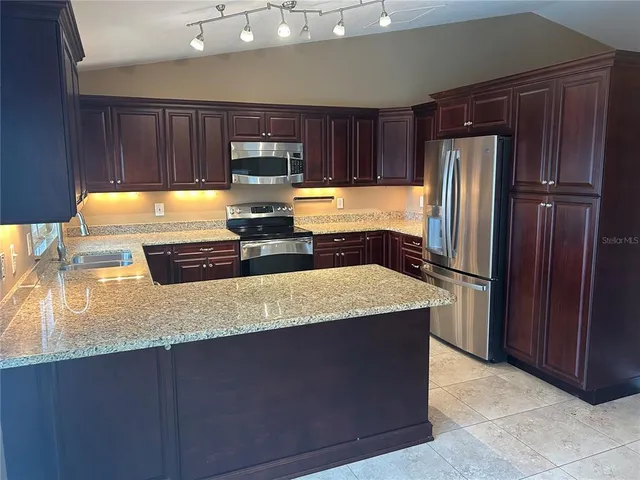 a kitchen with stainless steel appliances granite countertop a refrigerator a stove and a sink with wooden cabinets