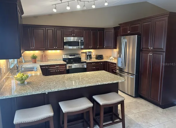 a kitchen with stainless steel appliances granite countertop a table chairs refrigerator and sink