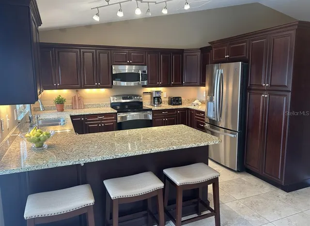 a kitchen with stainless steel appliances granite countertop a table chairs refrigerator and sink