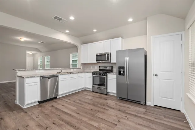 a large kitchen with a center island wooden floor stainless steel appliances and cabinets