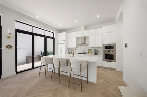 a large white kitchen with stainless steel appliances granite countertop a stove a sink a refrigerator and white cabinets with wooden floor