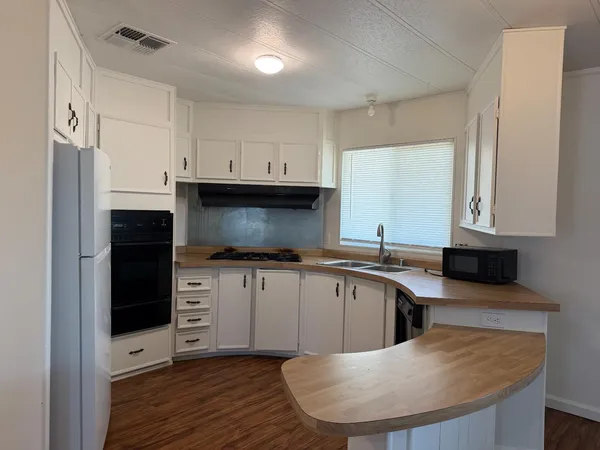 a view of empty room with wooden floor and kitchen view