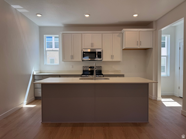 1472 North 1875 West, Unit 151 Layton, UT 84041 - Photo 4 of 20 Modern kitchen featuring a central island with an undermount sink, light-toned countertops, and white upper cabinetry