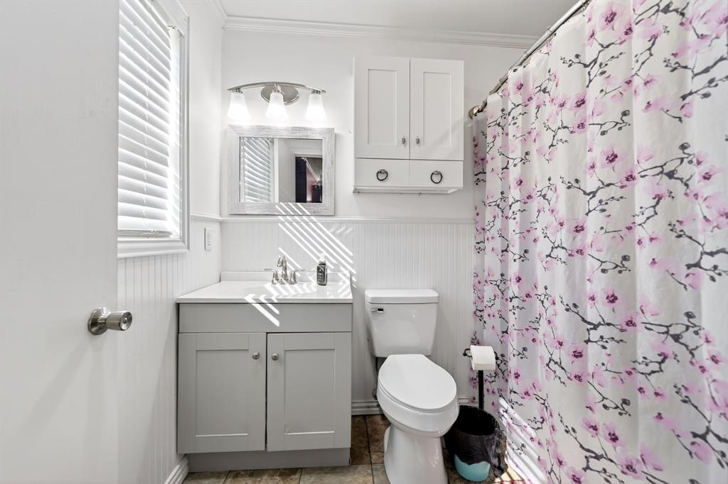 505 Laurel Road Athens, TX 75751 - Photo 21 of 32 Bathroom featuring a corner vanity with a light gray cabinet and white countertop, white beadboard wainscoting, white wall-mounted upper cabinets, and a window with white blinds