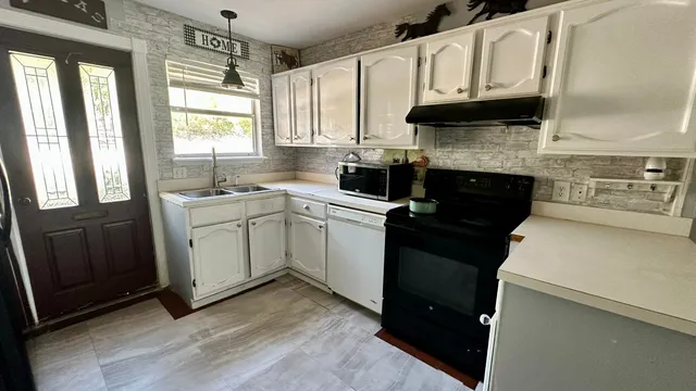 a kitchen with stainless steel appliances granite countertop white cabinets sink and a window