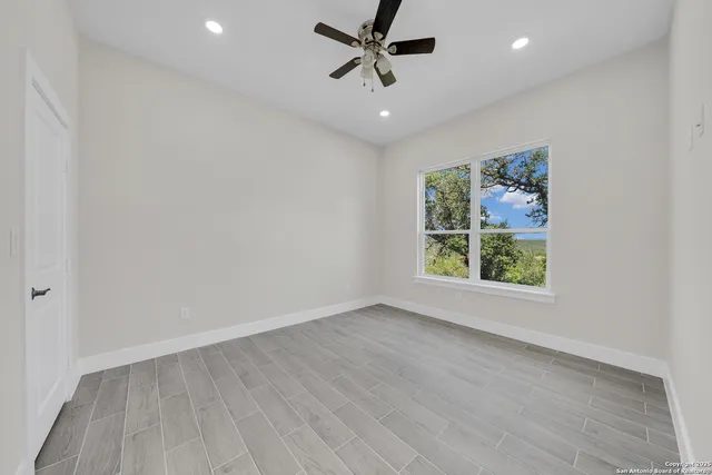 an empty room with wooden floor ceiling fan and windows