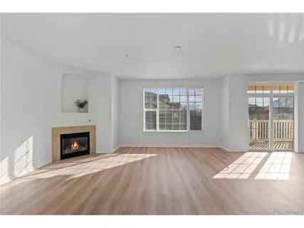 a view of an empty room with wooden floor fireplace and a window