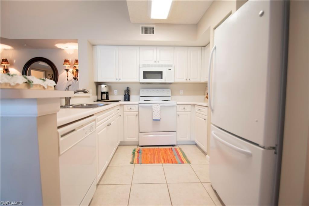 1220 Wildwood Lakes Boulevard, Unit 201 Naples, FL 34104 - Photo 18 of 35 Kitchen with white appliances, white cabinets, sink, light tile patterned floors, and kitchen peninsula