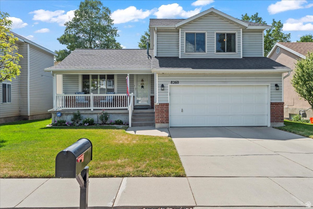 8260 South 560 East Sandy, UT 84070 - Photo 1 of 1 Traditional-style home featuring covered porch, a front yard, brick siding, and an attached garage