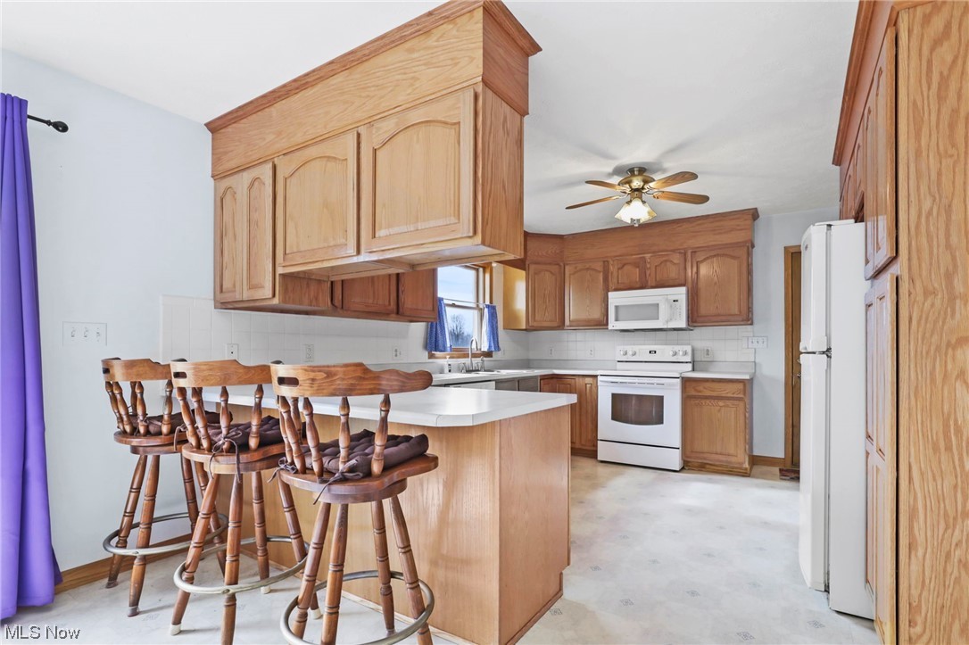 411 Adario West Road Shiloh, OH 44878 - Photo 7 of 35 Kitchen featuring a kitchen bar, kitchen peninsula, white appliances, tasteful backsplash, and ceiling fan