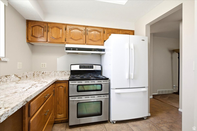 7050 South 260 East Midvale, UT 84047 - Photo 11 of 28 Kitchen featuring wood cabinetry, light-toned stone countertops, and a stainless steel double oven range with a coordinating vent hood