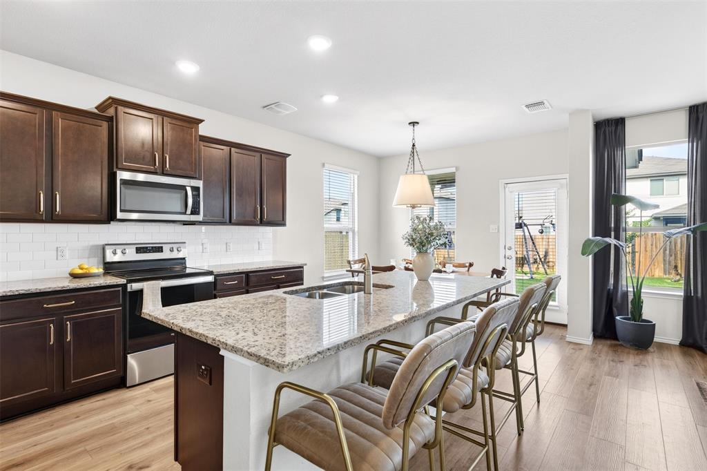 3105 Marston Road Lorena, TX 76655 - Photo 11 of 40 Open-concept kitchen featuring wood-finish flooring, dark wood cabinetry, a granite-finish island, stainless steel appliances, and white subway tile backsplash