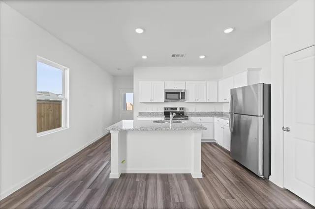 a kitchen with stainless steel appliances a refrigerator a sink dishwasher a oven with white cabinets and wooden floor