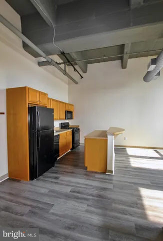 a view of a refrigerator in kitchen and an empty room with wooden floor