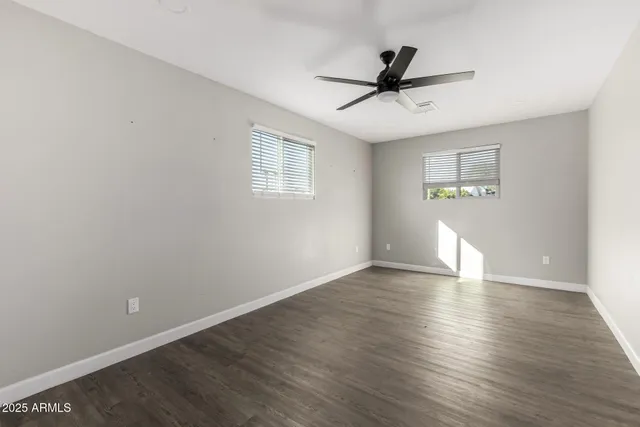 an empty room with wooden floor ceiling fan and windows