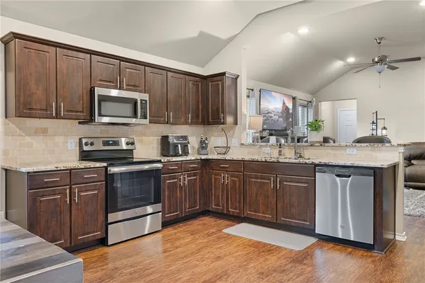a kitchen with stainless steel appliances granite countertop a stove a sink dishwasher and a microwave oven with wooden cabinets