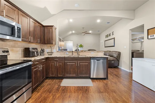 a kitchen with stainless steel appliances granite countertop wooden cabinets a sink a stove a microwave and wooden floors